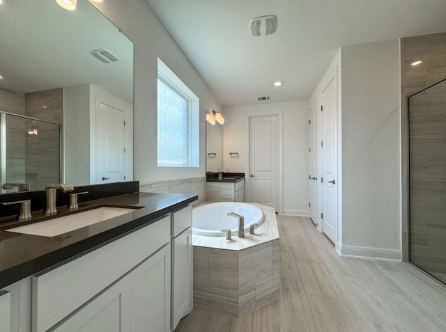 bathroom featuring visible vents, two vanities, a stall shower, a bath, and a sink