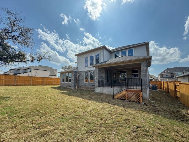 rear view of house featuring a fenced backyard, a lawn, stone siding, and stucco siding