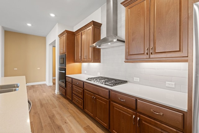 kitchen with light wood-type flooring, appliances with stainless steel finishes, wall chimney range hood, and backsplash