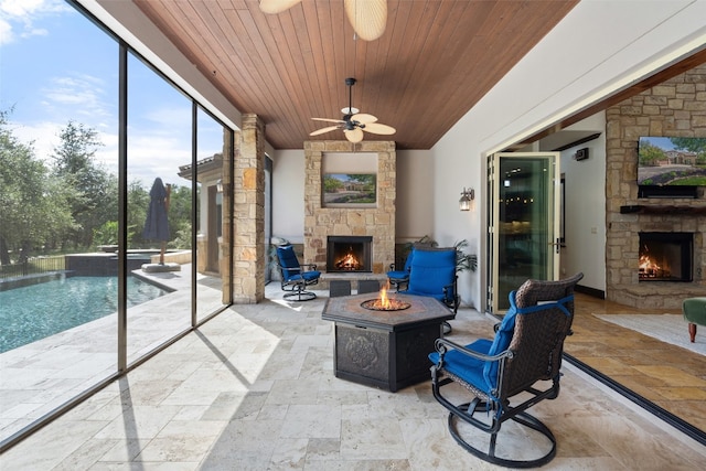 sunroom featuring a stone fireplace, ceiling fan, and wooden ceiling