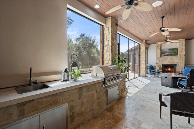 view of patio with an outdoor fire pit, sink, an outdoor stone fireplace, ceiling fan, and area for grilling