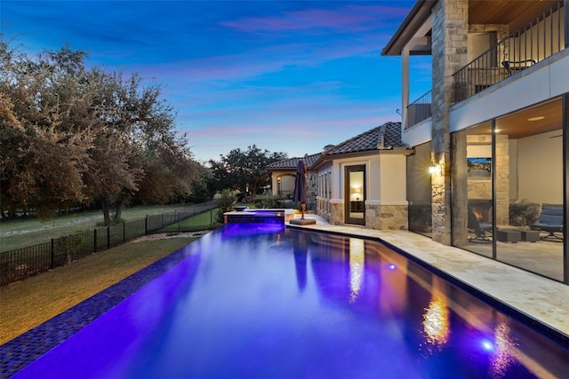 pool at dusk featuring a patio area and an in ground hot tub