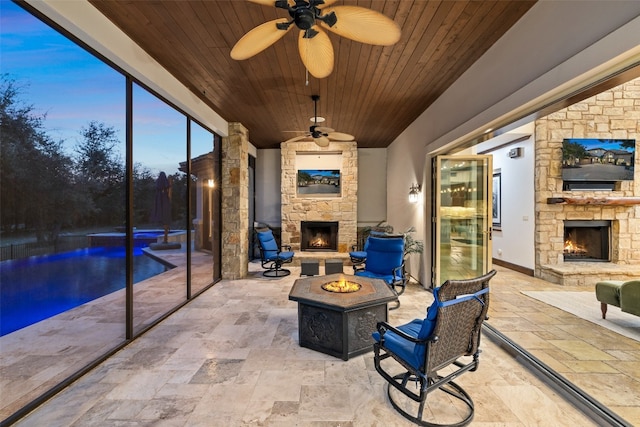 unfurnished sunroom featuring ceiling fan, wooden ceiling, and an outdoor stone fireplace