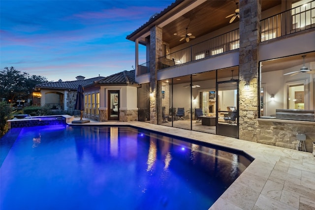 pool at dusk with ceiling fan, a patio, and an in ground hot tub