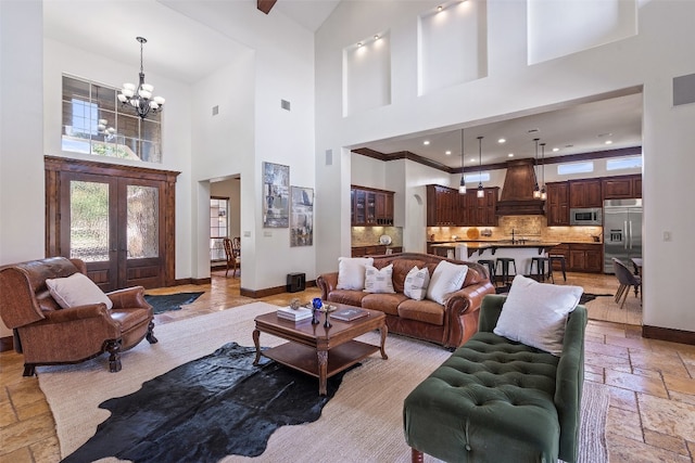 living room featuring french doors, crown molding, a towering ceiling, sink, and a chandelier