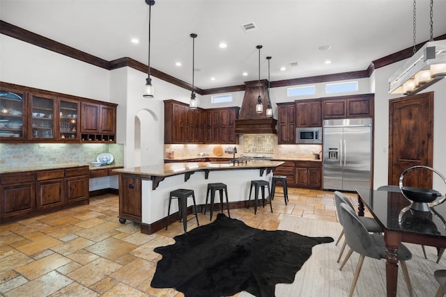 kitchen with decorative backsplash, pendant lighting, premium range hood, and built in appliances