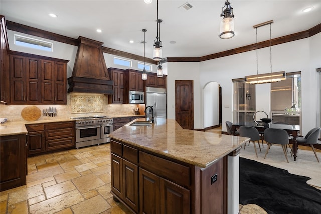 kitchen featuring built in appliances, a spacious island, sink, and decorative light fixtures