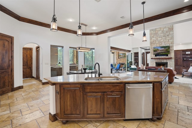 kitchen featuring a stone fireplace, a center island with sink, sink, light stone countertops, and decorative light fixtures