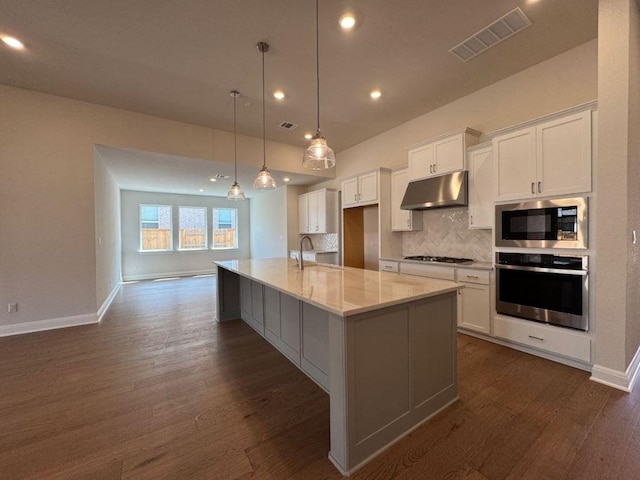 kitchen featuring oven, visible vents, under cabinet range hood, built in microwave, and decorative backsplash