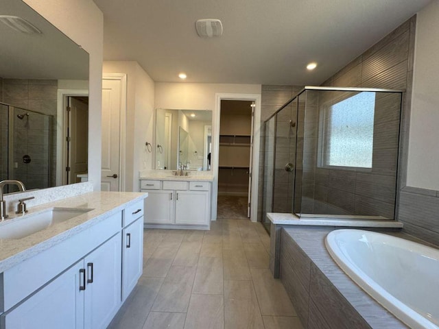 full bath featuring a bath, a stall shower, two vanities, and a sink