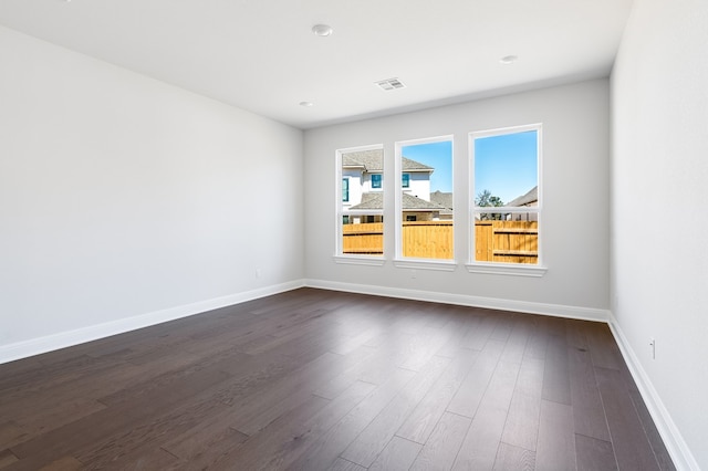 spare room featuring dark wood-type flooring, visible vents, and baseboards