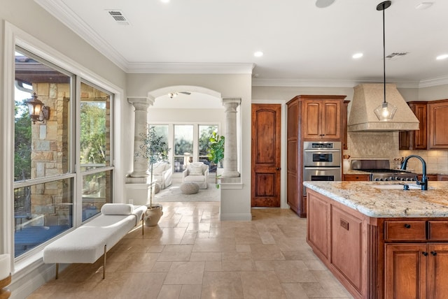 kitchen featuring ornate columns, light stone counters, premium range hood, double oven, and pendant lighting