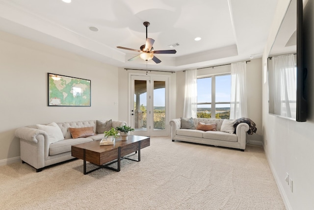 carpeted living room with plenty of natural light, ceiling fan, a raised ceiling, and french doors