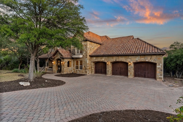 7409 Lantern View Dr, Jonestown, TX 78645 - mediterranean / spanish home featuring stone siding, a tile roof, decorative driveway, and an attached garage