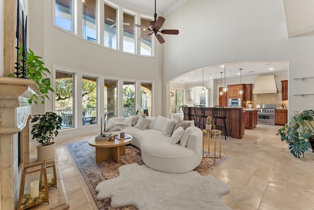 living room with a towering ceiling, ceiling fan, and crown molding