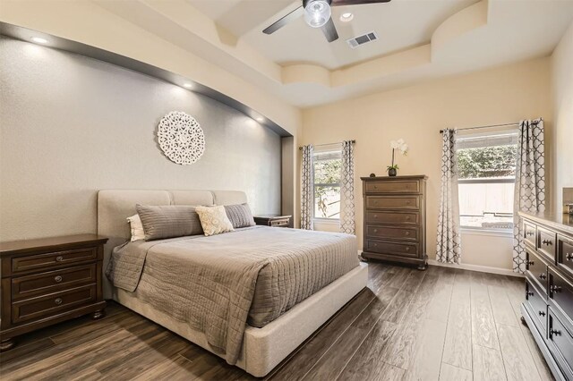 bedroom with dark wood-type flooring, ceiling fan, and a raised ceiling