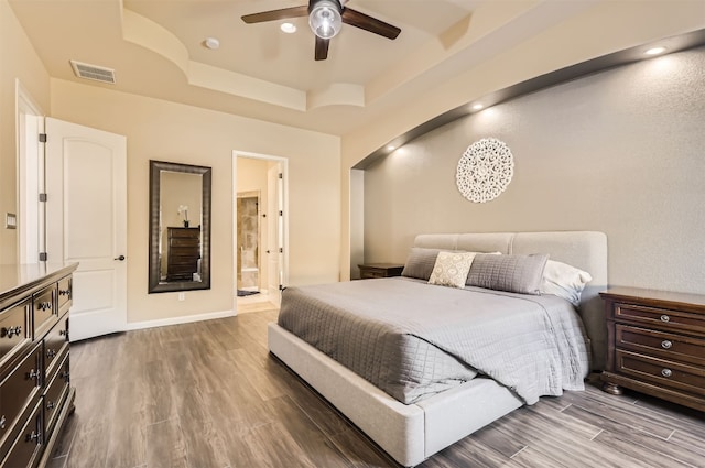 bedroom featuring hardwood / wood-style flooring, ceiling fan, connected bathroom, and a tray ceiling