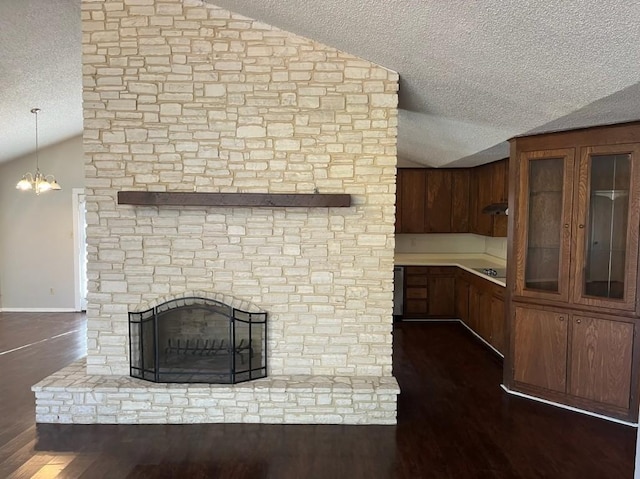 unfurnished living room featuring a textured ceiling, a stone fireplace, dark hardwood / wood-style flooring, and vaulted ceiling