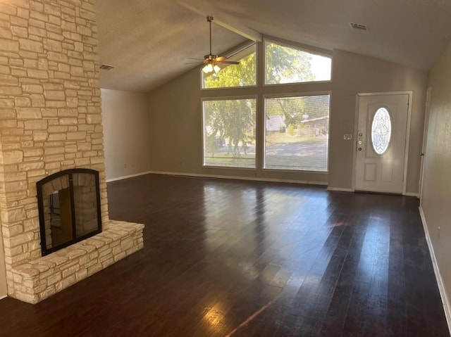 unfurnished living room with a textured ceiling, vaulted ceiling, ceiling fan, dark hardwood / wood-style floors, and a stone fireplace