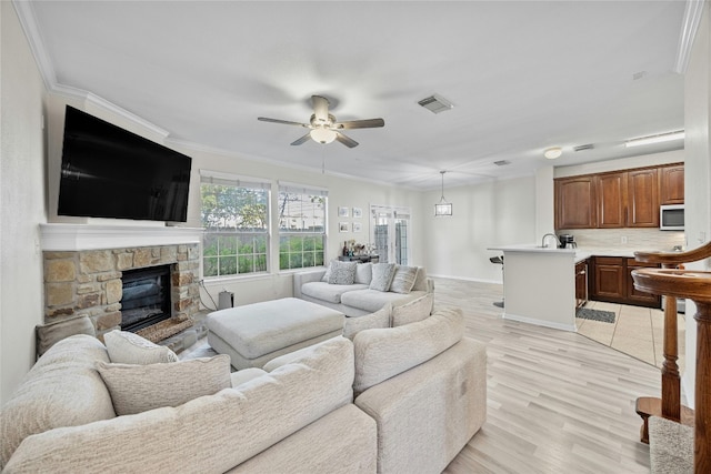 living room with ornamental molding, a stone fireplace, sink, light hardwood / wood-style floors, and ceiling fan