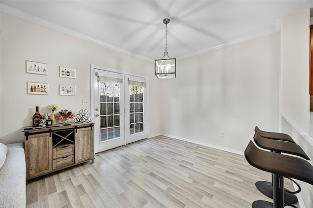 dining room with ornamental molding, light wood-type flooring, french doors, and an inviting chandelier