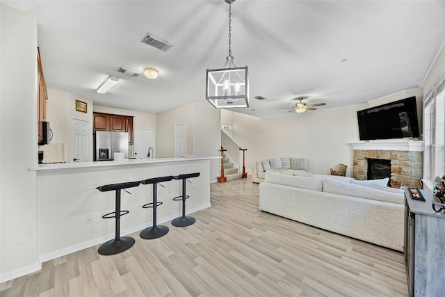 living room featuring a stone fireplace, sink, light hardwood / wood-style floors, and ceiling fan with notable chandelier