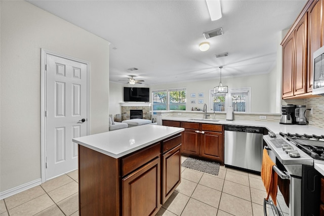 kitchen featuring stainless steel appliances, a center island, hanging light fixtures, backsplash, and a fireplace