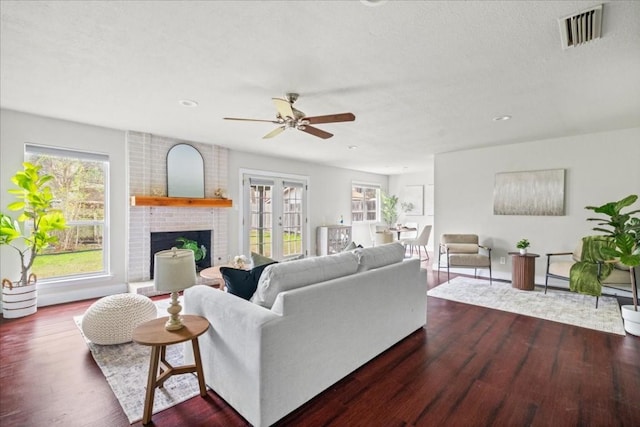 living room featuring ceiling fan, a healthy amount of sunlight, dark hardwood / wood-style floors, and a fireplace