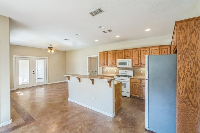 kitchen featuring an island with sink, white appliances, a kitchen bar, and concrete flooring