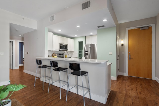 kitchen featuring a kitchen bar, stainless steel appliances, dark wood-type flooring, kitchen peninsula, and white cabinetry