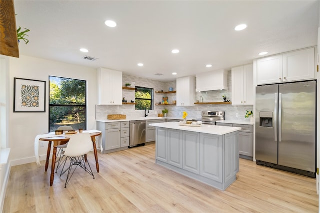 kitchen featuring a center island, stainless steel appliances, light hardwood / wood-style floors, decorative backsplash, and custom range hood