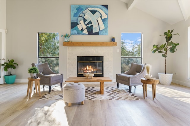 living area with high vaulted ceiling, a tile fireplace, light wood-type flooring, and beamed ceiling