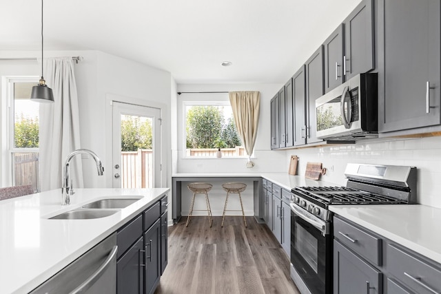 kitchen featuring stainless steel appliances, a sink, light countertops, gray cabinets, and tasteful backsplash