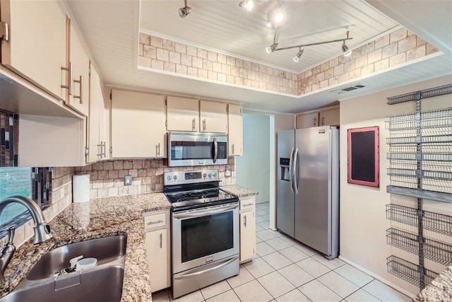 kitchen with backsplash, track lighting, light stone counters, stainless steel appliances, and sink