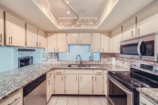 kitchen featuring sink, stainless steel appliances, light stone counters, track lighting, and cream cabinetry