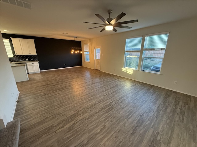 unfurnished living room featuring ceiling fan with notable chandelier and dark hardwood / wood-style floors