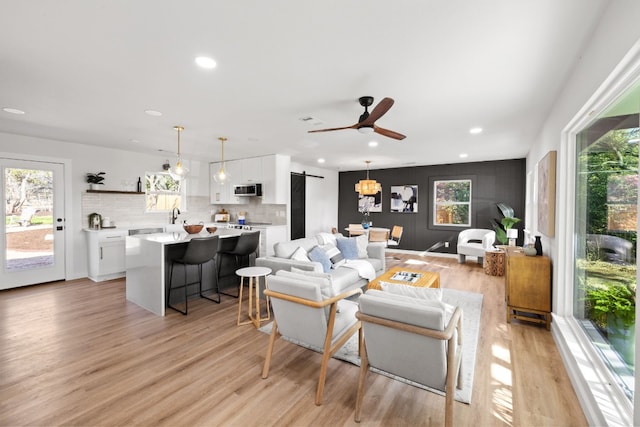 living room with a barn door, light hardwood / wood-style flooring, ceiling fan, and sink