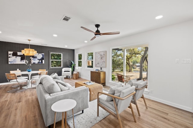 living room with ceiling fan with notable chandelier, light wood-type flooring, and wooden walls