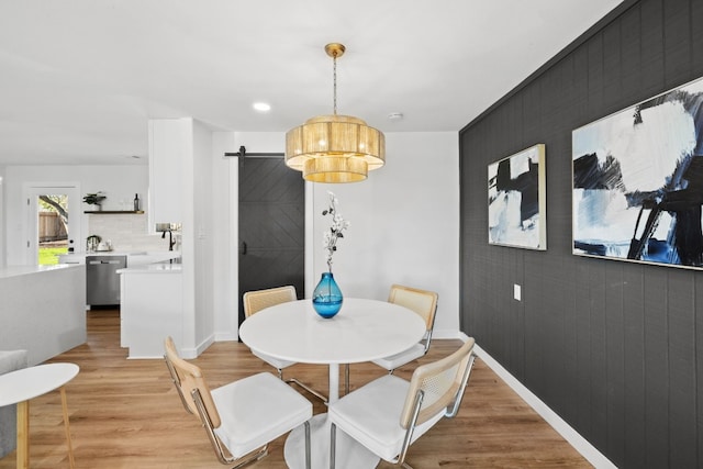 dining area with a barn door, sink, and light hardwood / wood-style floors