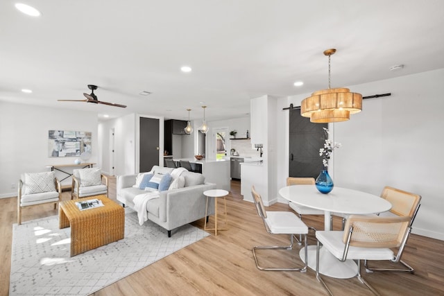 living room featuring light hardwood / wood-style floors, ceiling fan, and a barn door