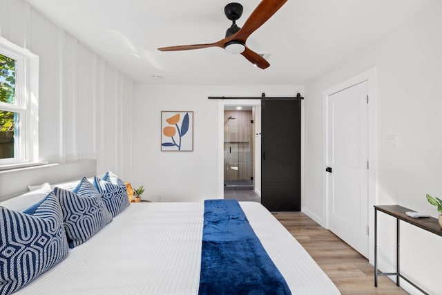 bedroom with a barn door, hardwood / wood-style flooring, ceiling fan, and connected bathroom