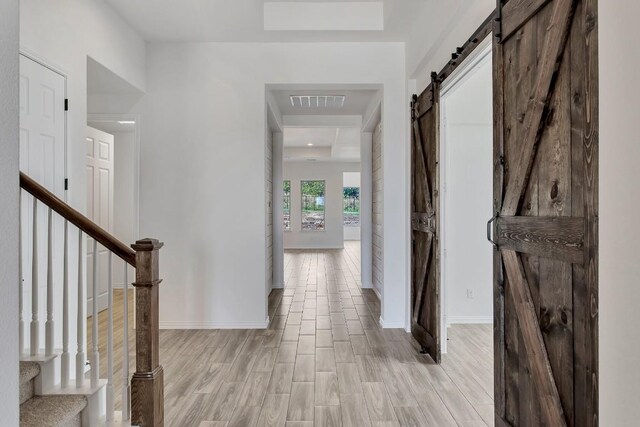 hall with a barn door, light hardwood / wood-style floors, and a raised ceiling