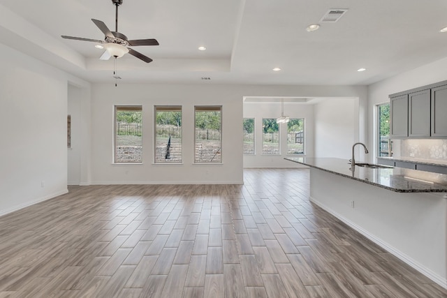 unfurnished living room featuring a raised ceiling, light hardwood / wood-style flooring, ceiling fan, and sink