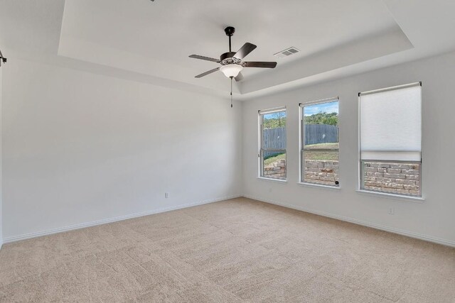 unfurnished room featuring ceiling fan, a raised ceiling, and light colored carpet