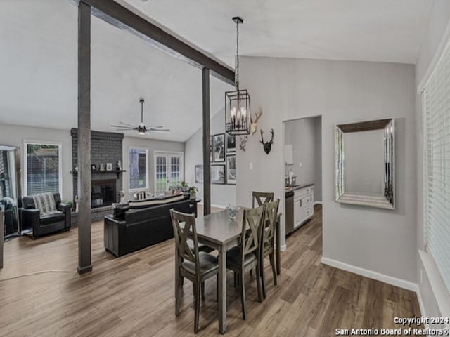 dining room with a brick fireplace, ceiling fan with notable chandelier, lofted ceiling, and hardwood / wood-style flooring