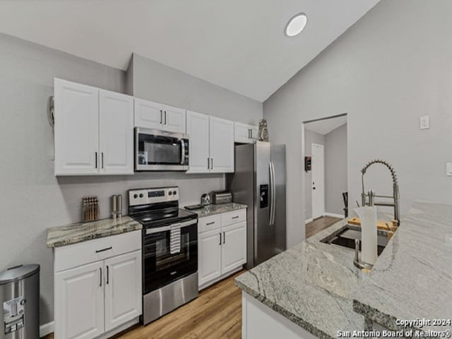 kitchen featuring light stone countertops, white cabinetry, stainless steel appliances, and lofted ceiling