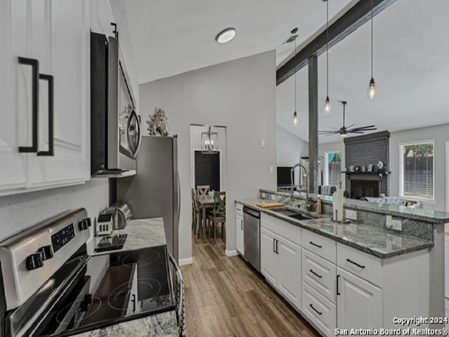 kitchen with dark stone counters, decorative light fixtures, lofted ceiling, white cabinets, and appliances with stainless steel finishes