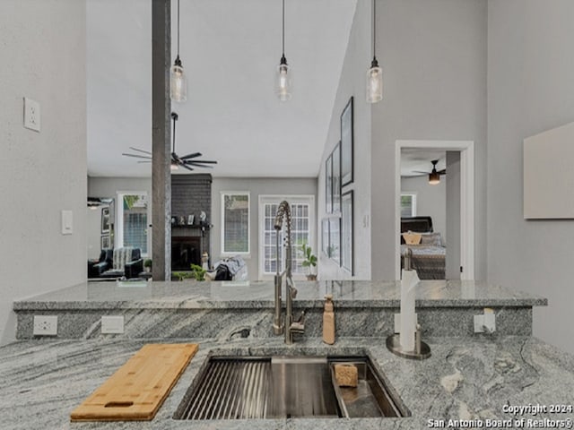 kitchen featuring a fireplace, pendant lighting, light stone countertops, and sink