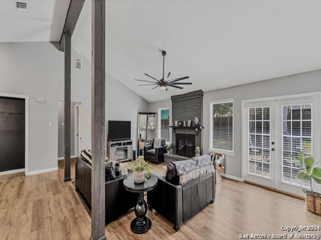 living room with light hardwood / wood-style flooring, vaulted ceiling, a brick fireplace, and french doors