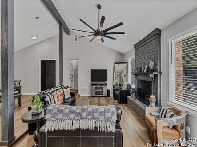 living room featuring vaulted ceiling with beams, light hardwood / wood-style floors, a brick fireplace, and ceiling fan